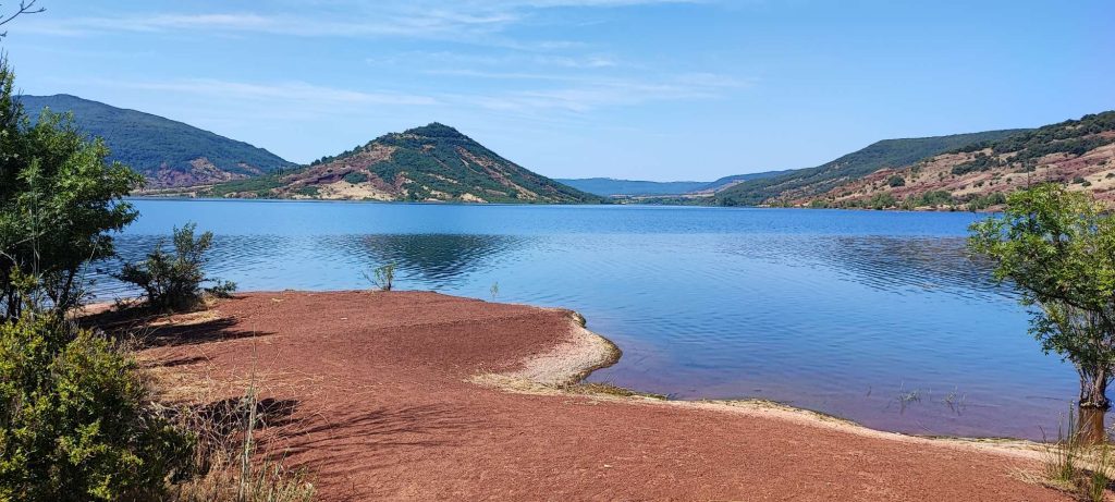 Photo du Lac du Salagou depuis la rive nord ou se combine les couleurs rouge de la terre, bleu de l'eau et du ciel, vert de la végétation