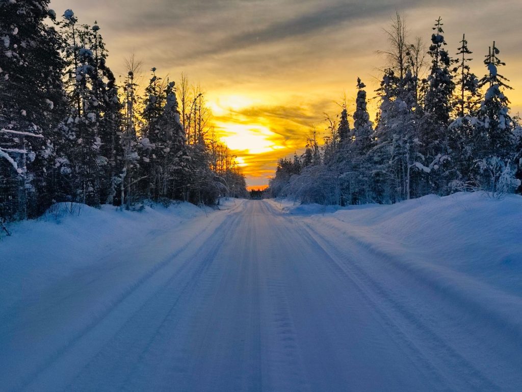 Photo d'une route enneigée bordée de sapin au coucher du soleil en Laponie Finlandaise